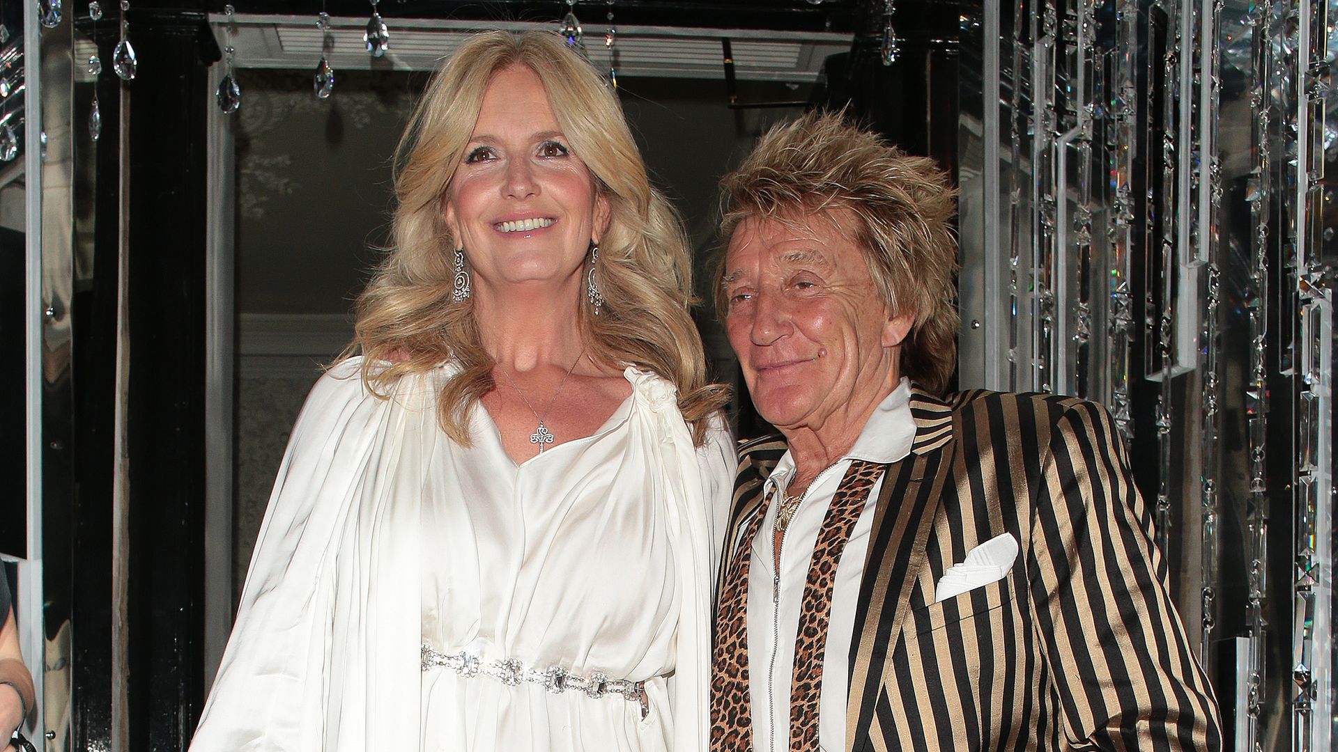 Penny Lancaster in white mini dress with Rod Stewart in a golden-striped suit