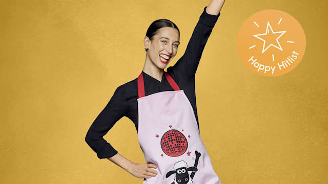 Laura Jackson wearing shaun the sheep apron with hand up on yellow backdrop
