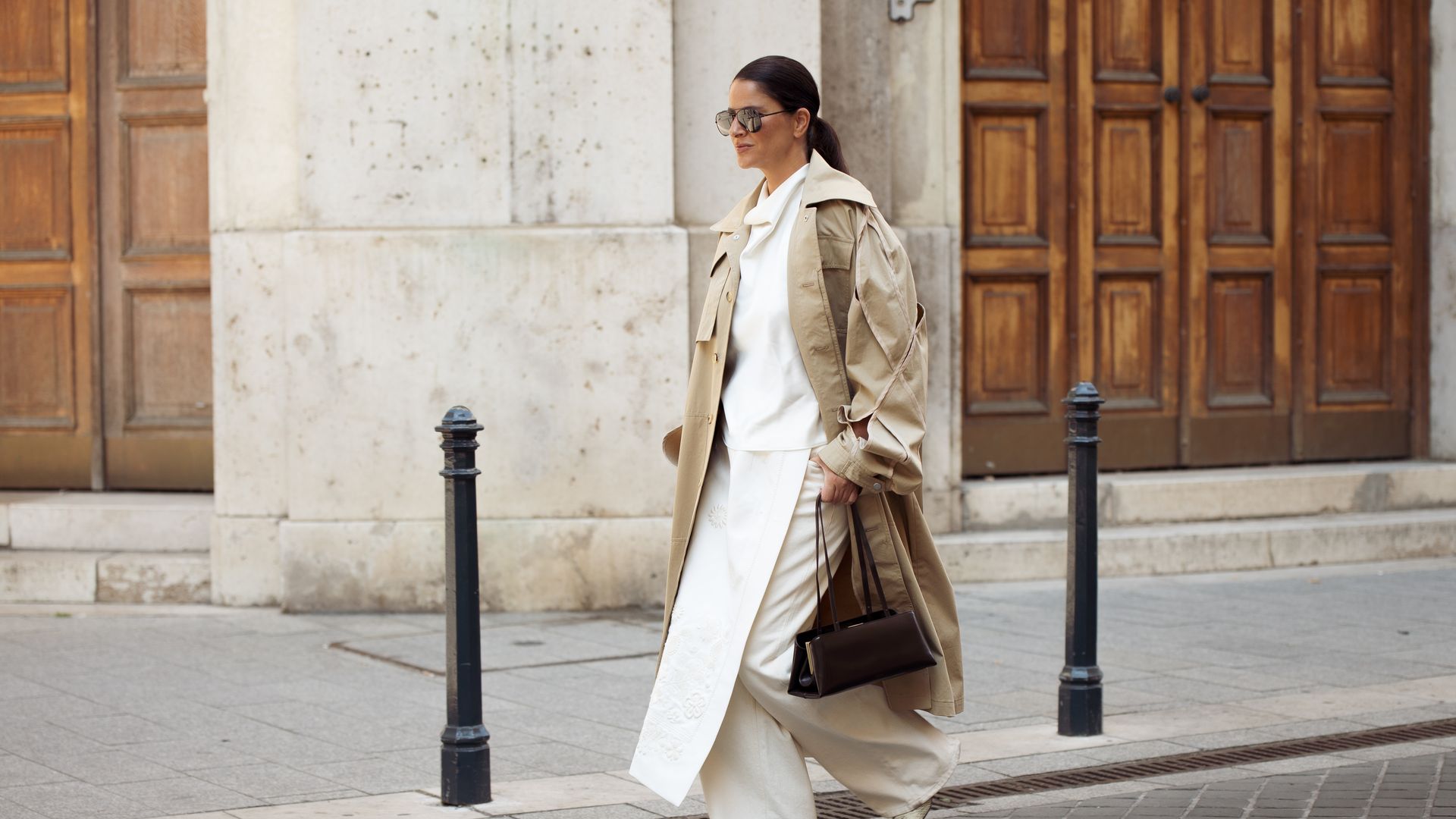 BUDAPEST, HUNGARY - SEPTEMBER 07: Gili Biegun wears beige long trench coat with sleeves details, white Silk halter neck top, cream and white apron skirt over cream white jeans, brown leather shoulder bag and snake skin print leather boots during the Budapest Central European Fashion Week (BCEFW ) SS26 on September 07, 2025 in Budapest, Hungary. (Photo by Raimonda Kulikauskiene/Getty Images)