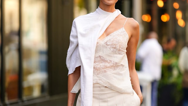 Chriselle Lim wears black sunglasses from Fendi, gold embossed cut-out logo earrings from Fendi, a white wool scarf, a white embossed lace pattern V-neck / backless / silk tank-top, white latte wide legs suit pants with embroidered pleated / accordion short skirt belt from Fendi, a dark brown shiny leather Peekaboo handbag from Fendi, outside Fendi, during the Haute Couture Fall/Winter 2023/2024