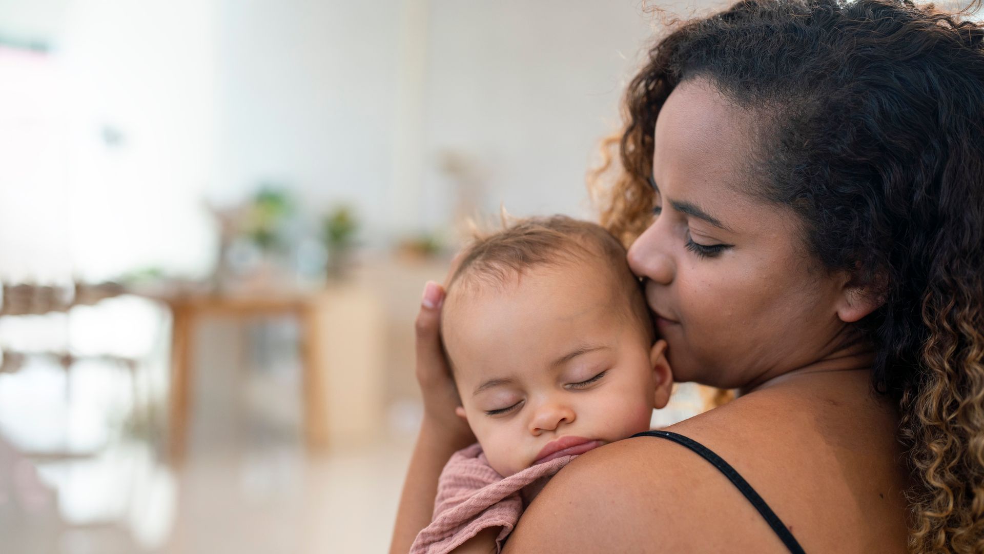 Close Up Of Mother Cuddling Sleeping Baby Daughter At Home