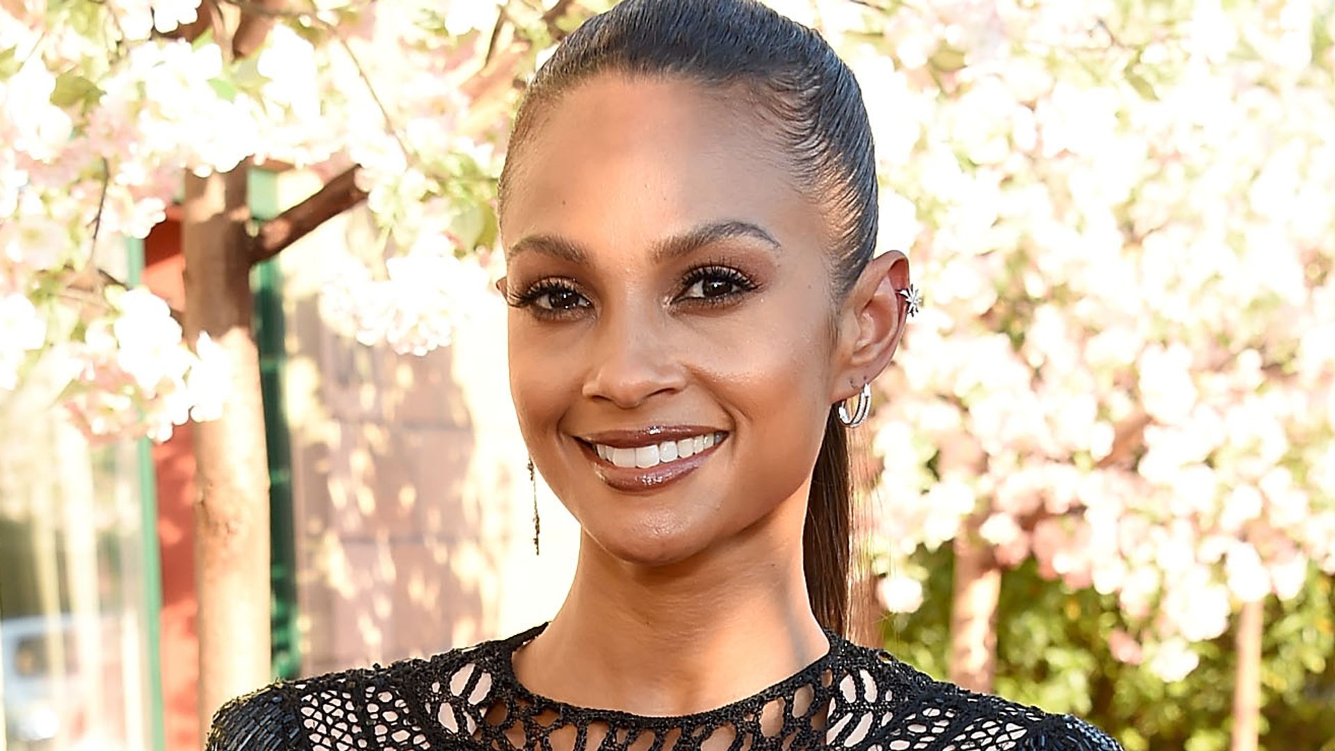 Alesha Dixon in a black dress with white flowers in the background