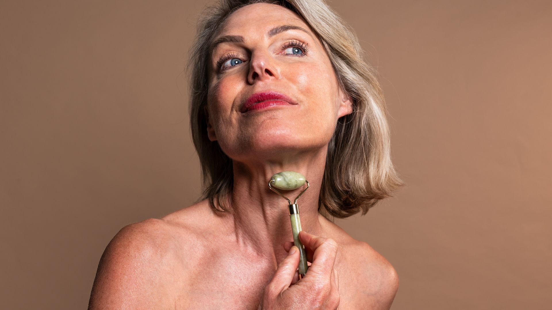 woman using jade roller on neck.