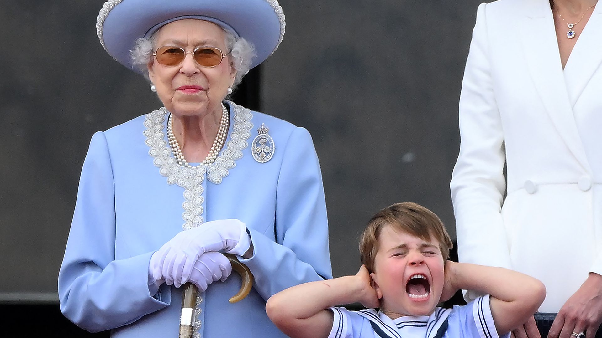 Prince Louis shouting and covering his ears while standing next to the Queen