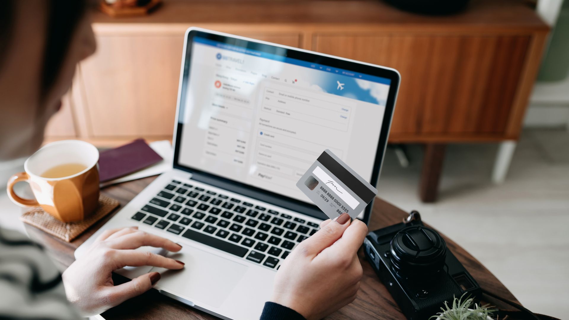 Over the shoulder view of young Asian woman shopping online for flight tickets on airline website with laptop, entering credit card details to make mobile payment at home