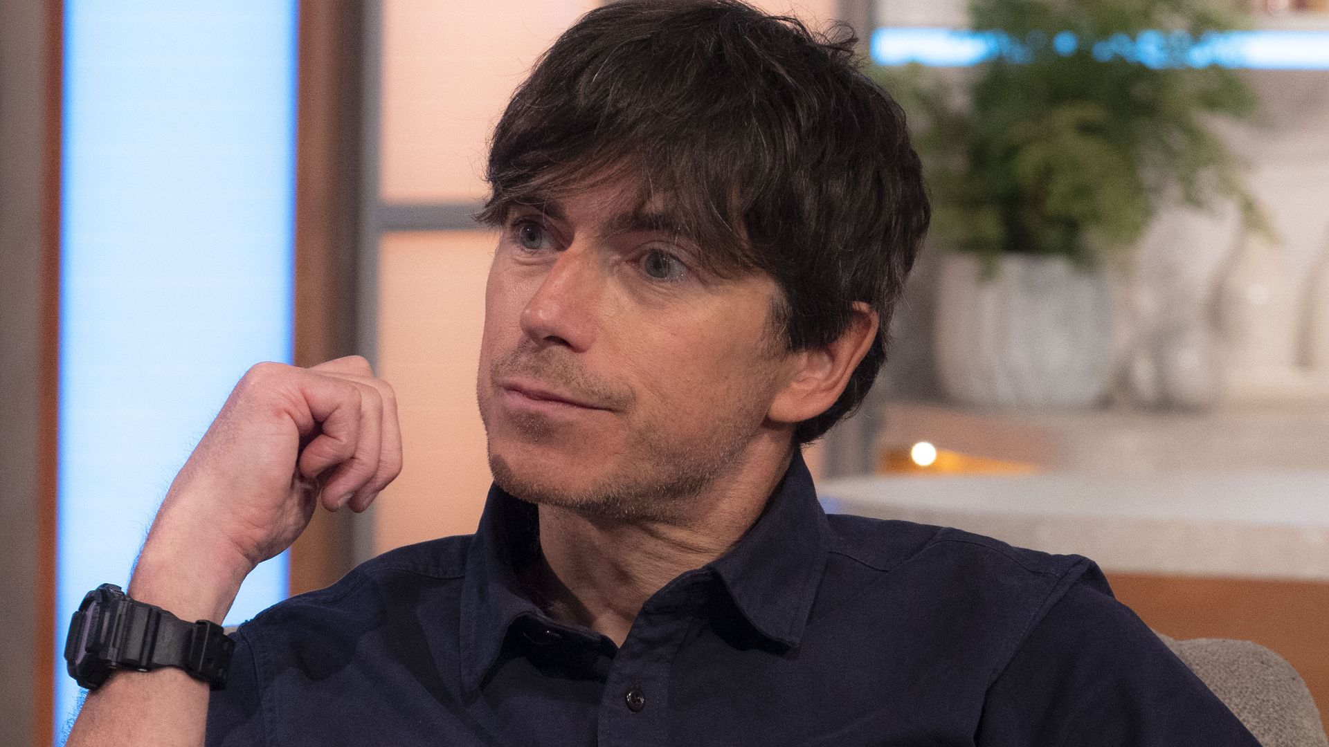 Simon Reeve in a blue shirt sitting in an armchair