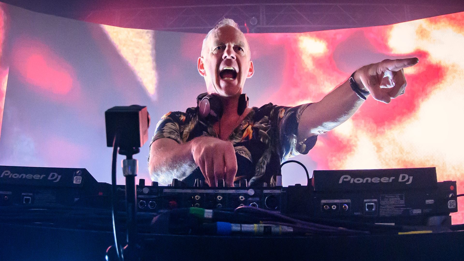 Fatboy Slim stood at a mixing deck pointing to the crowd and singing along