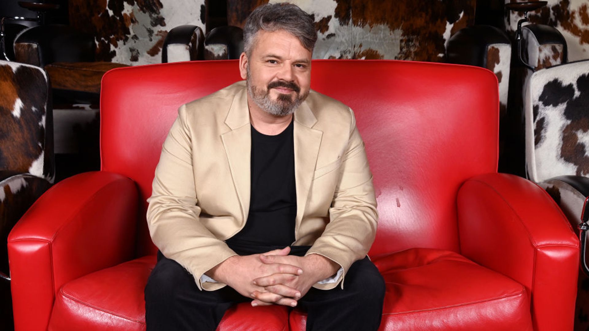 The late Paul Cattermole sitting on a red leather sofa. 