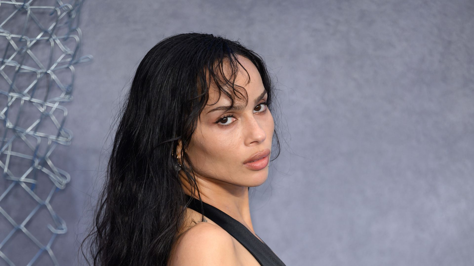 Zoë Kravitz in her amazing Saint Laurent dress on the red carpet. She looks to the side - her tattooes on her arms showcased, and her long tousled black hair with a slight wave