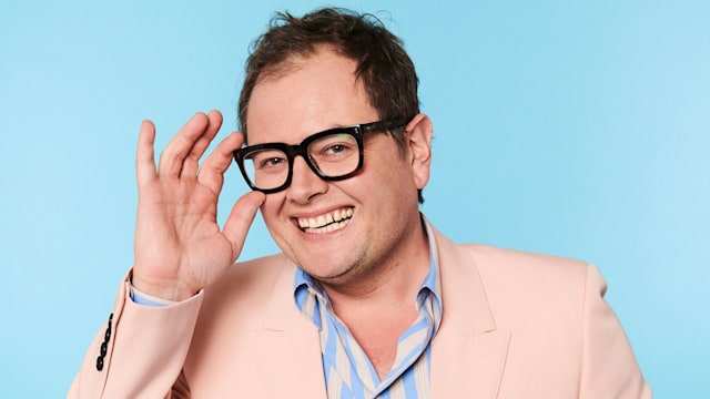 Alan Carr smiling whilst touching his glasses