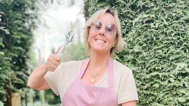 Shirlie Kemp smiling and holding up her toolbox with her garden in the background