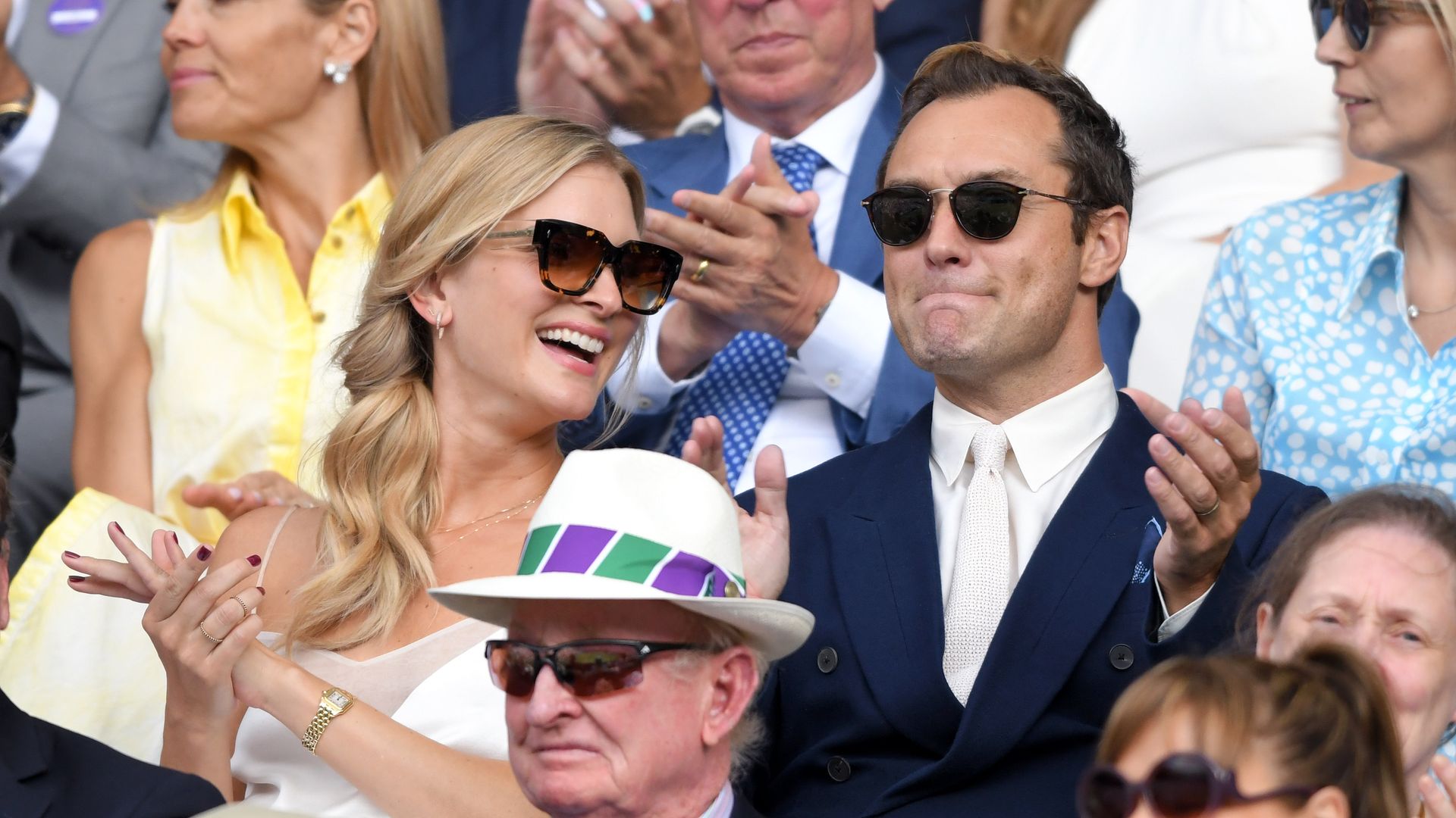 Jude and Phillipa sat watching Wimbledon, both are wearing sunglasses and clapping