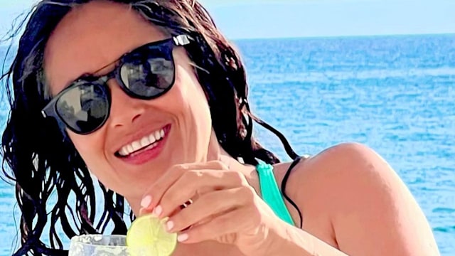 Salma Hayek wearing blue swimsuit drinking cocktail