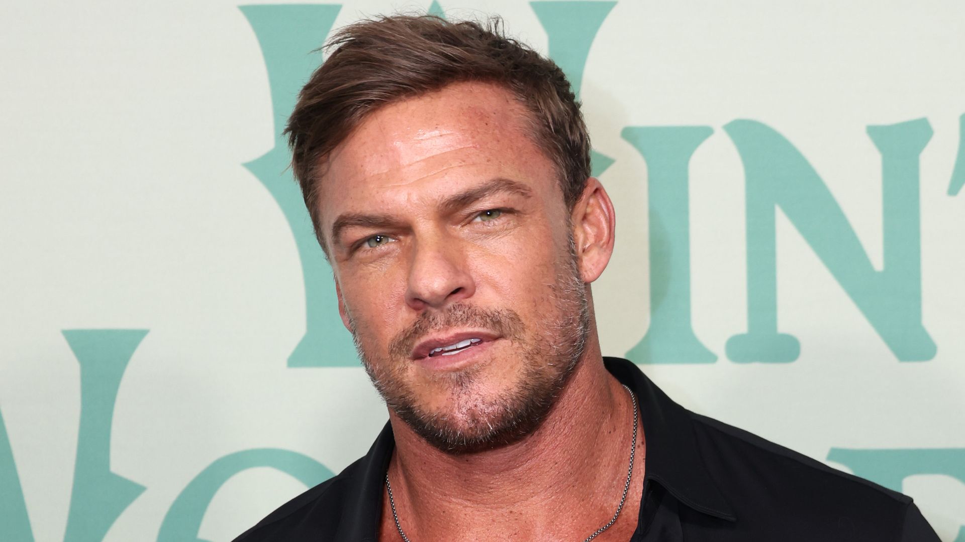 Alan Ritchson black shirt unbuttoned, muscular physique