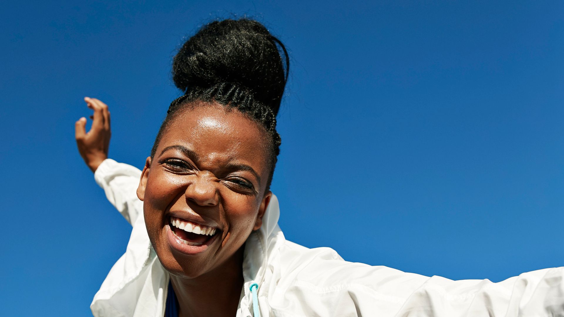 Portrait of cheerful young woman with hair bun wearing jacket and sports clothing during sunny day