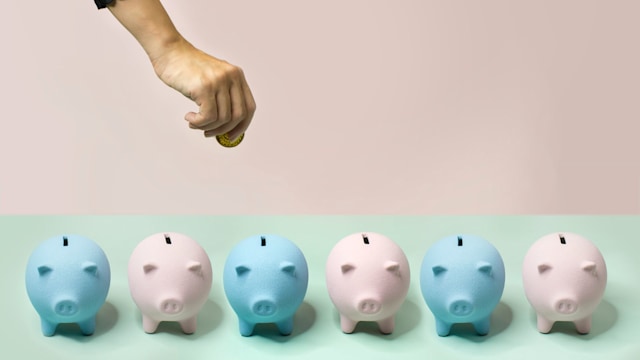 Hand putting coin into one of the many piggy banks on pastel coloured background.