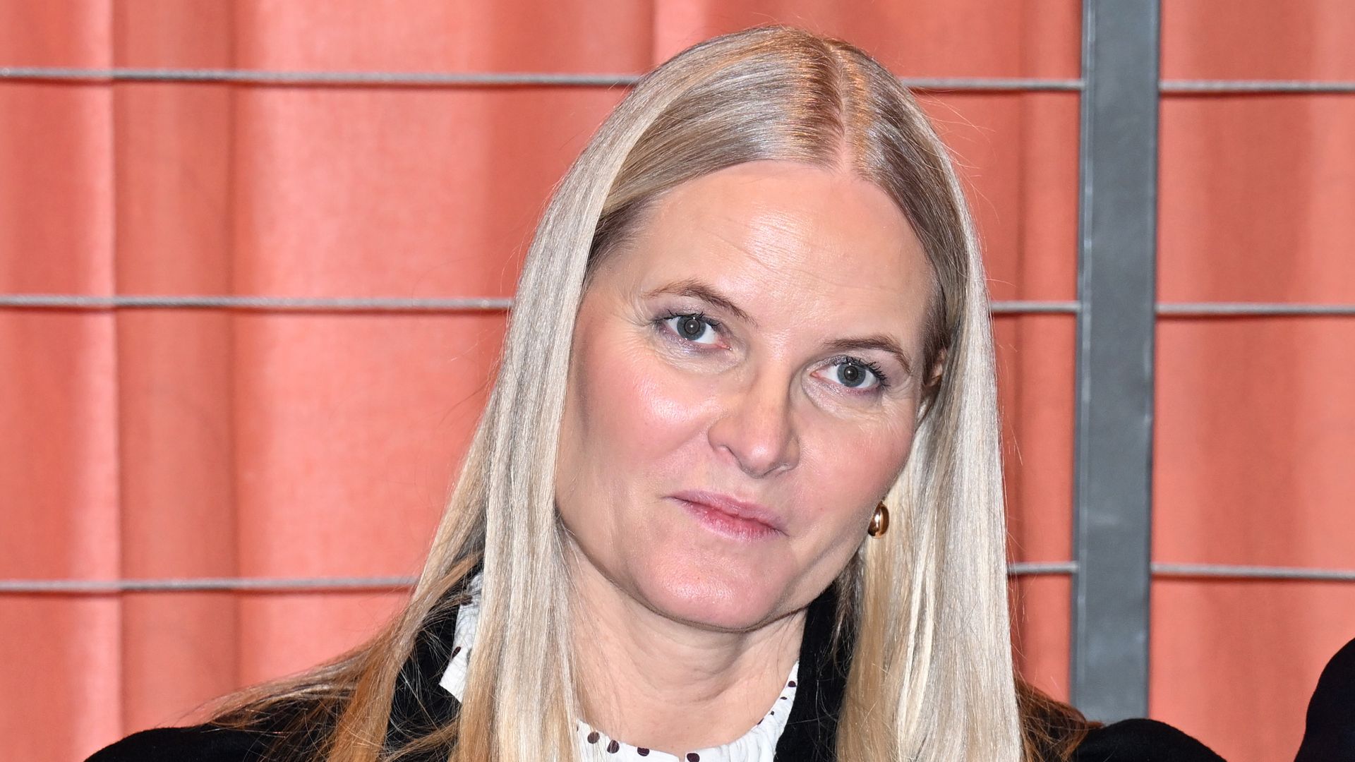 Princess Mette-Marit sitting in a black blazer and white spotted top