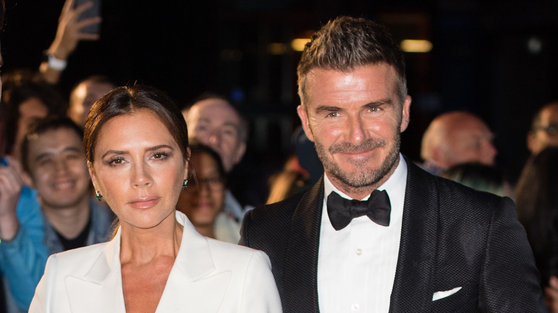 Victoria Beckham in white outfit stood with David Beckham in a suit