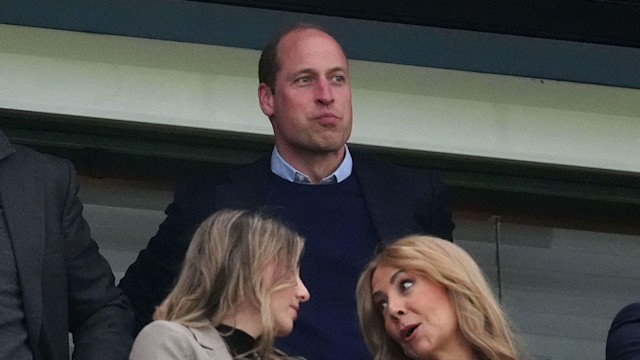 Prince William at a football match; two women are talking in front of him