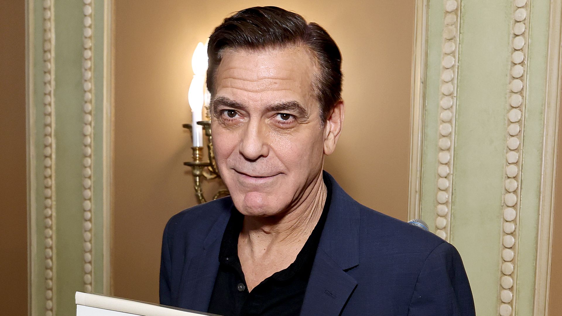 George Clooney holding his portait from Sardi and smiling for camera