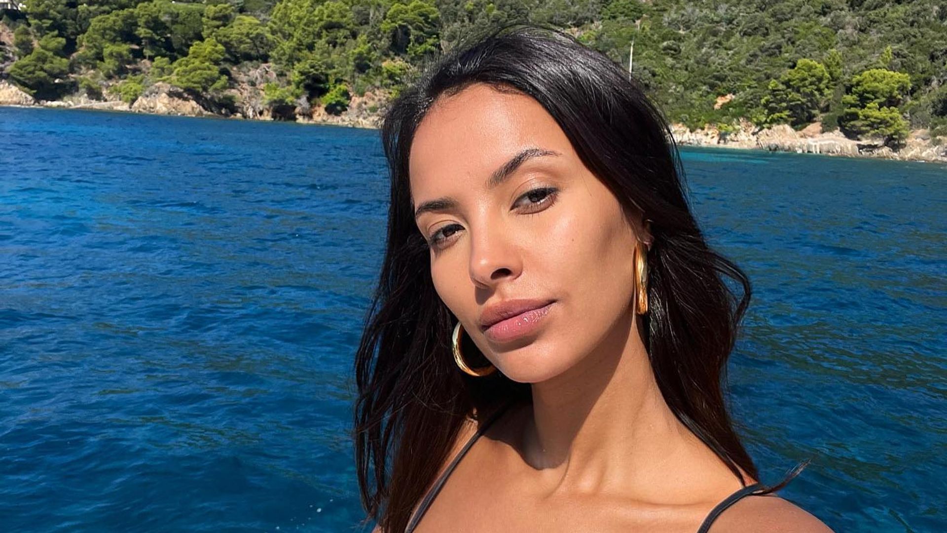 Maya Jama poses for a selfie in a bikini while sitting infront of the ocean