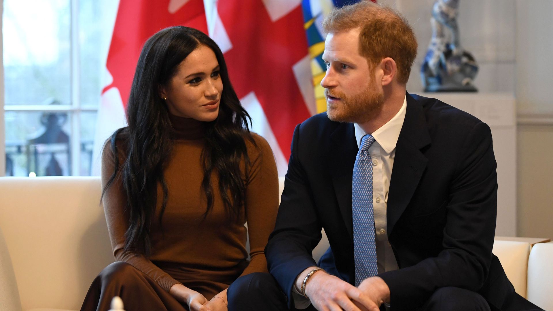 Harry and Meghan looking serious on a sofa