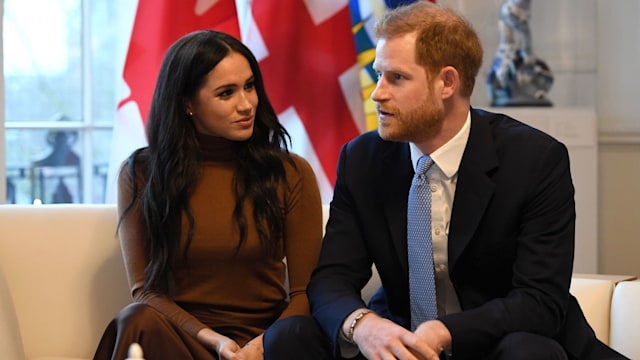 Harry and Meghan looking serious on a sofa