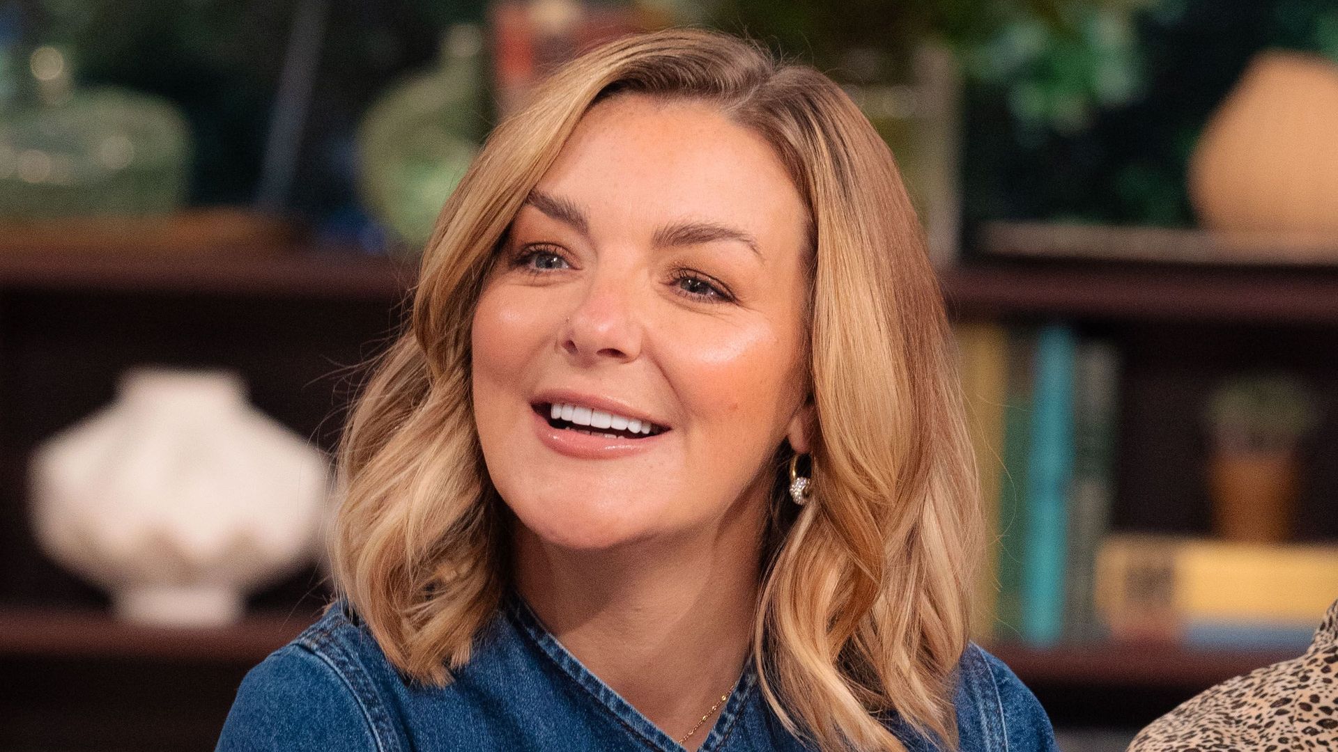 blonde woman in denim dress in tv studio on blue sofa