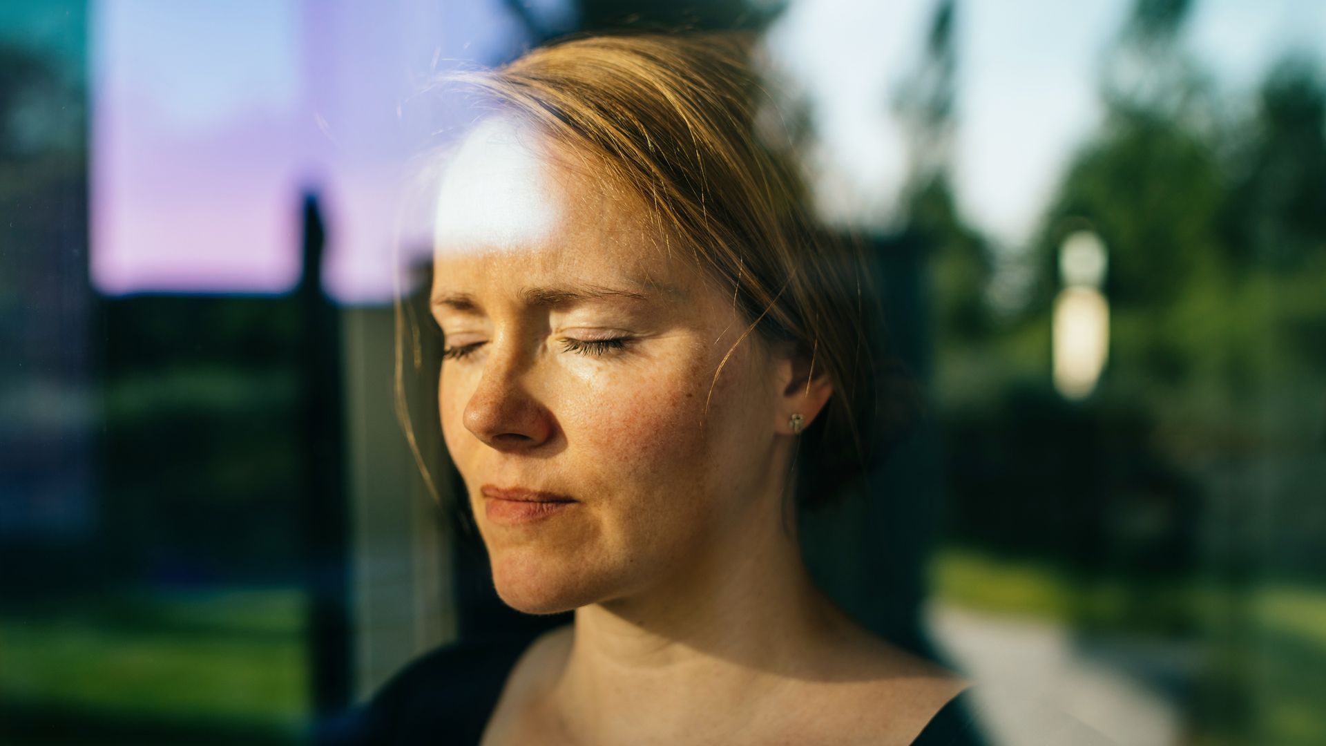 A contemplative woman with eyes closed in soft sunlight, symbolising introspection and emotional healing during a therapy journey.