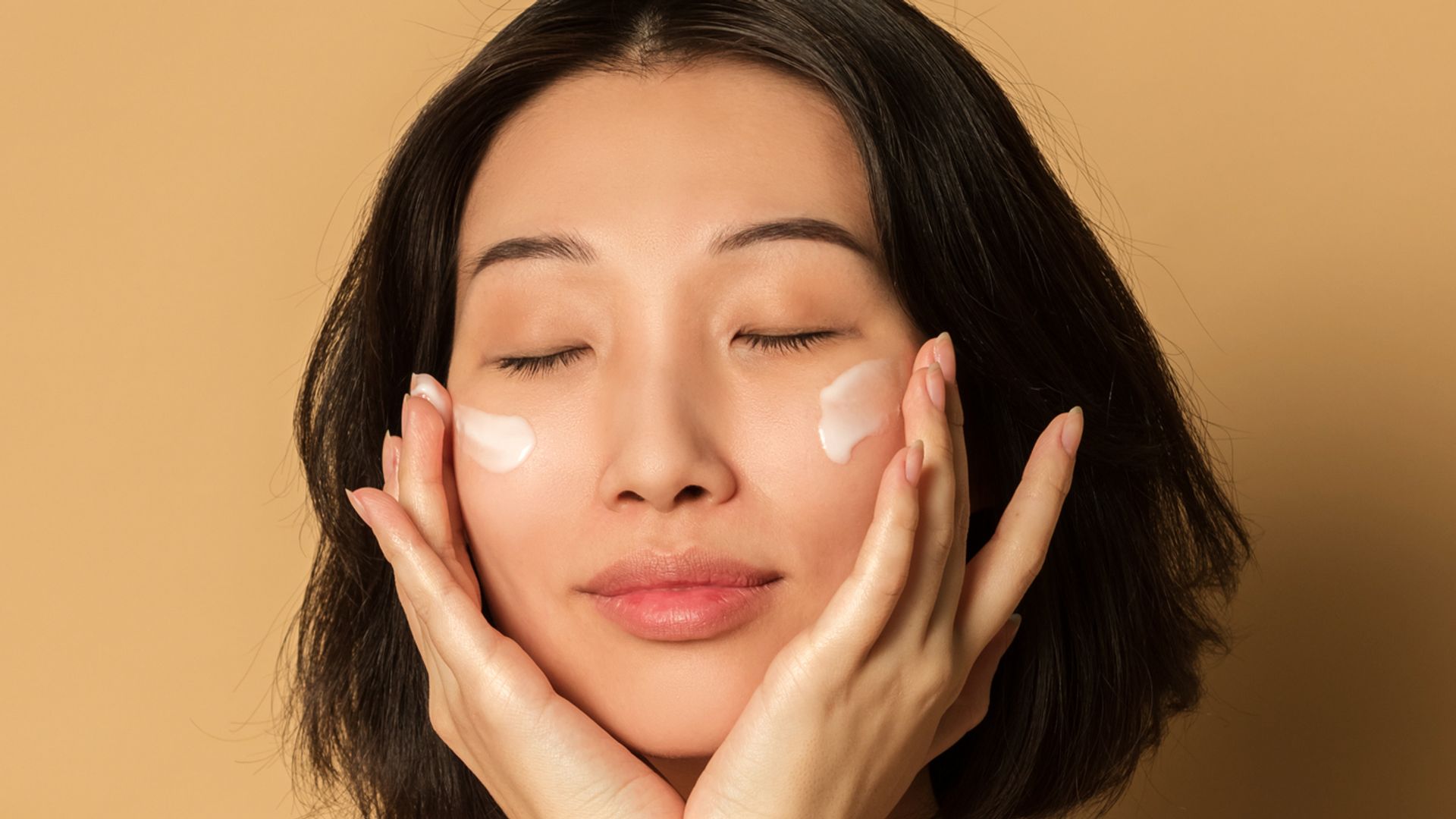 beautiful woman smears face cream on beige background studio shot beauty portrait