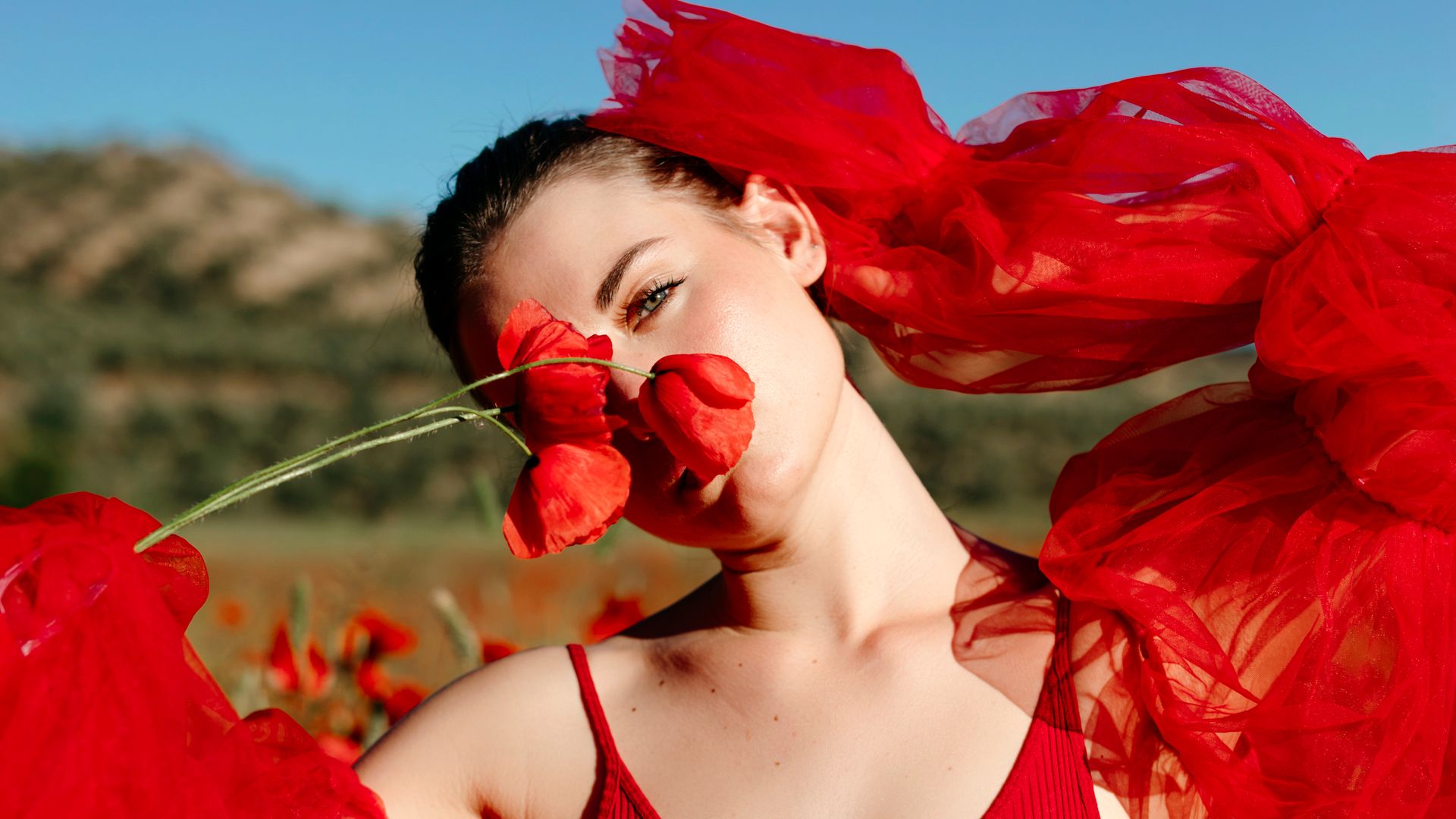woman sniffing a flower in a field in a red top