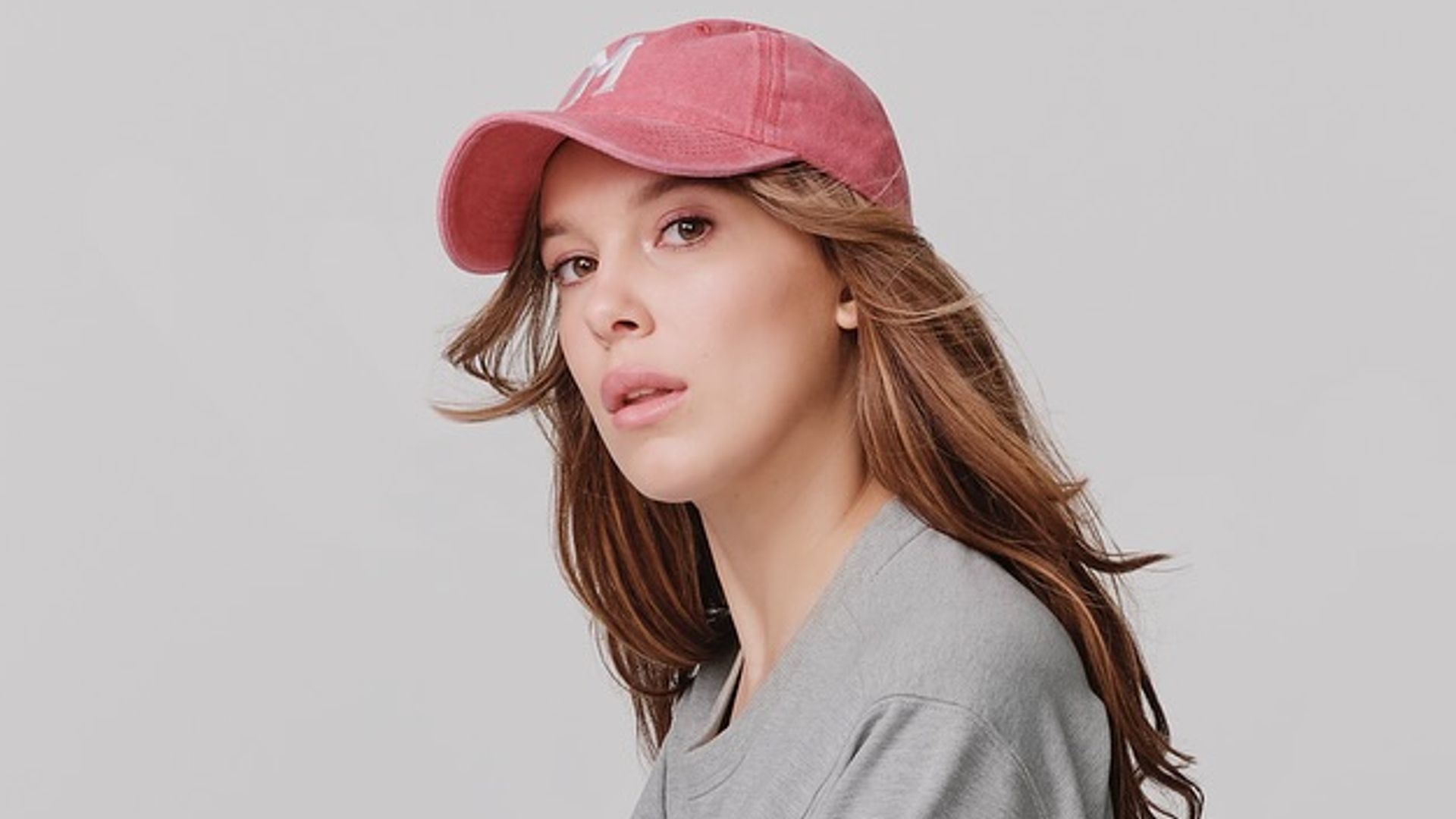Millie Bobby Brown poses in a cap and grey sweater