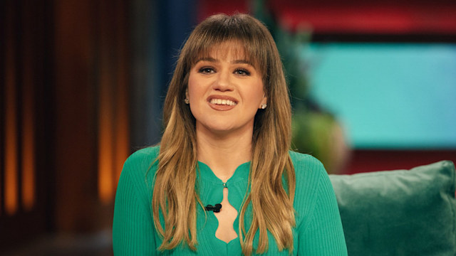 kelly clarkson in green dress sitting in chair on talk show stage