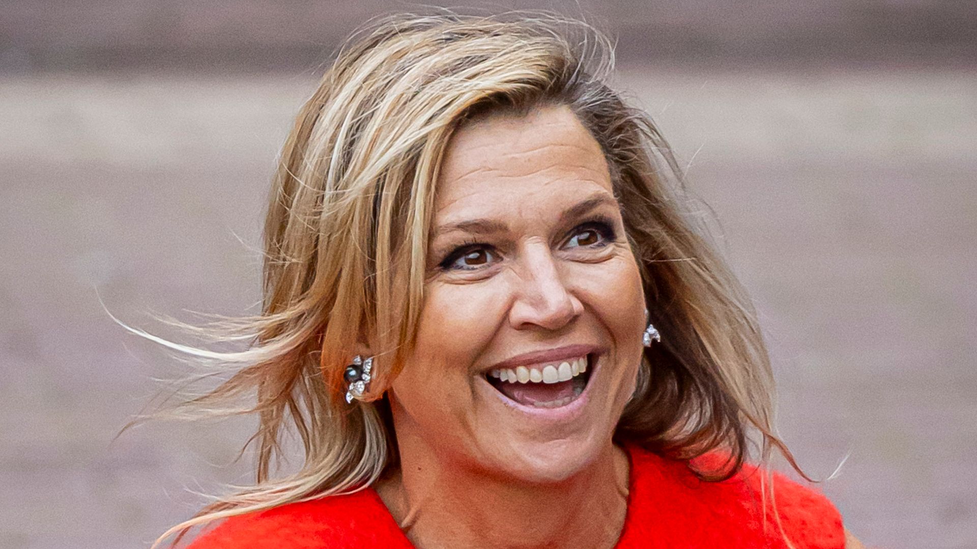 Queen Maxima in fuzzy orange top and grey trousers smiling