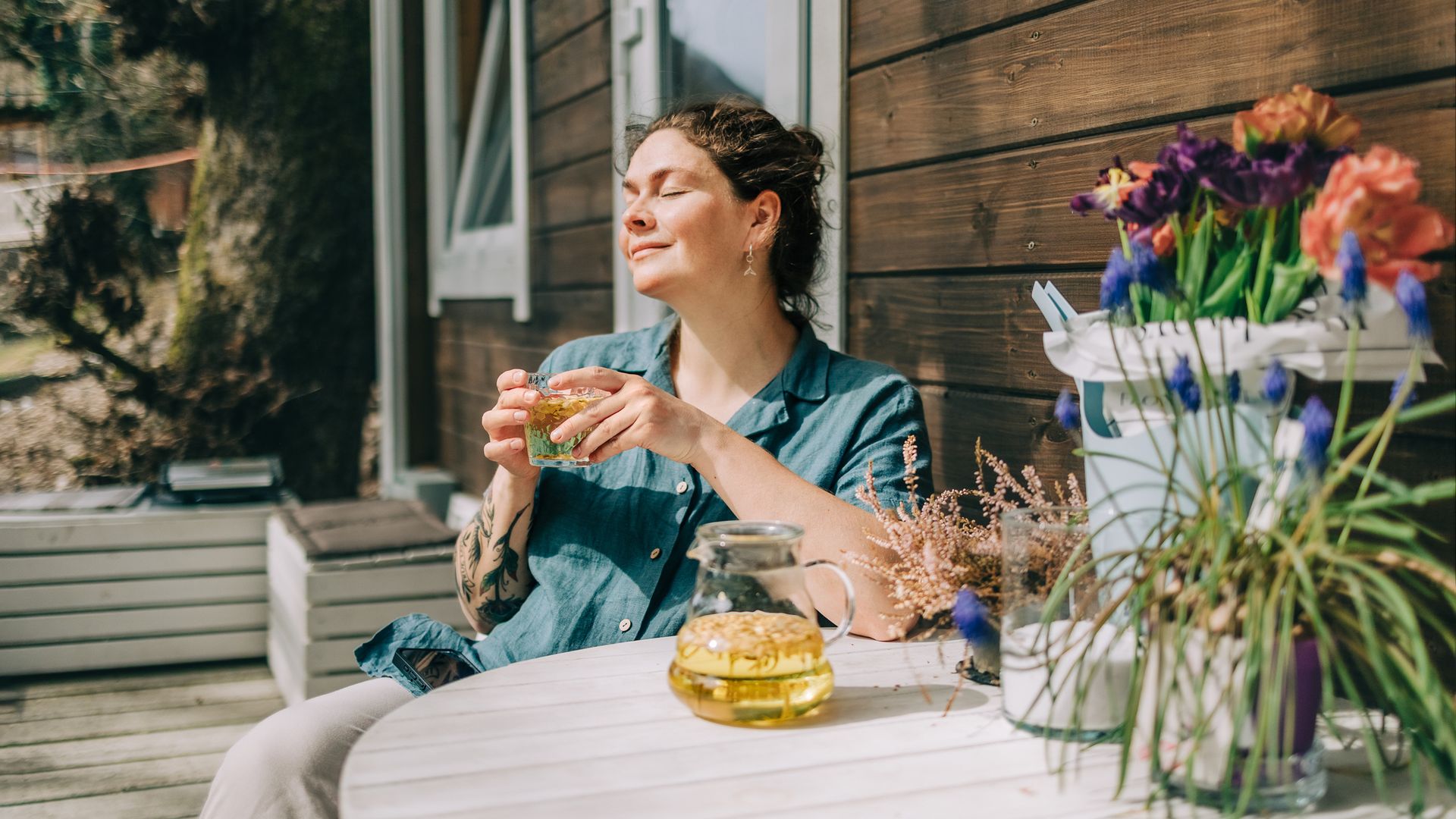 Woman relaxing with herbal tea on porch of wooden cottage