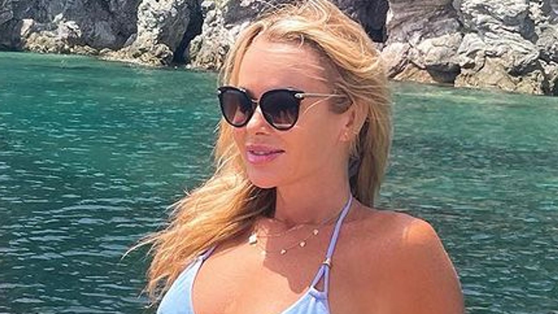 Amanda Holden wearing blue bikini and sunglasses sitting on boat