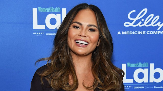 photo of chrissy teigen smiling wearing black top and mint green split skirt
