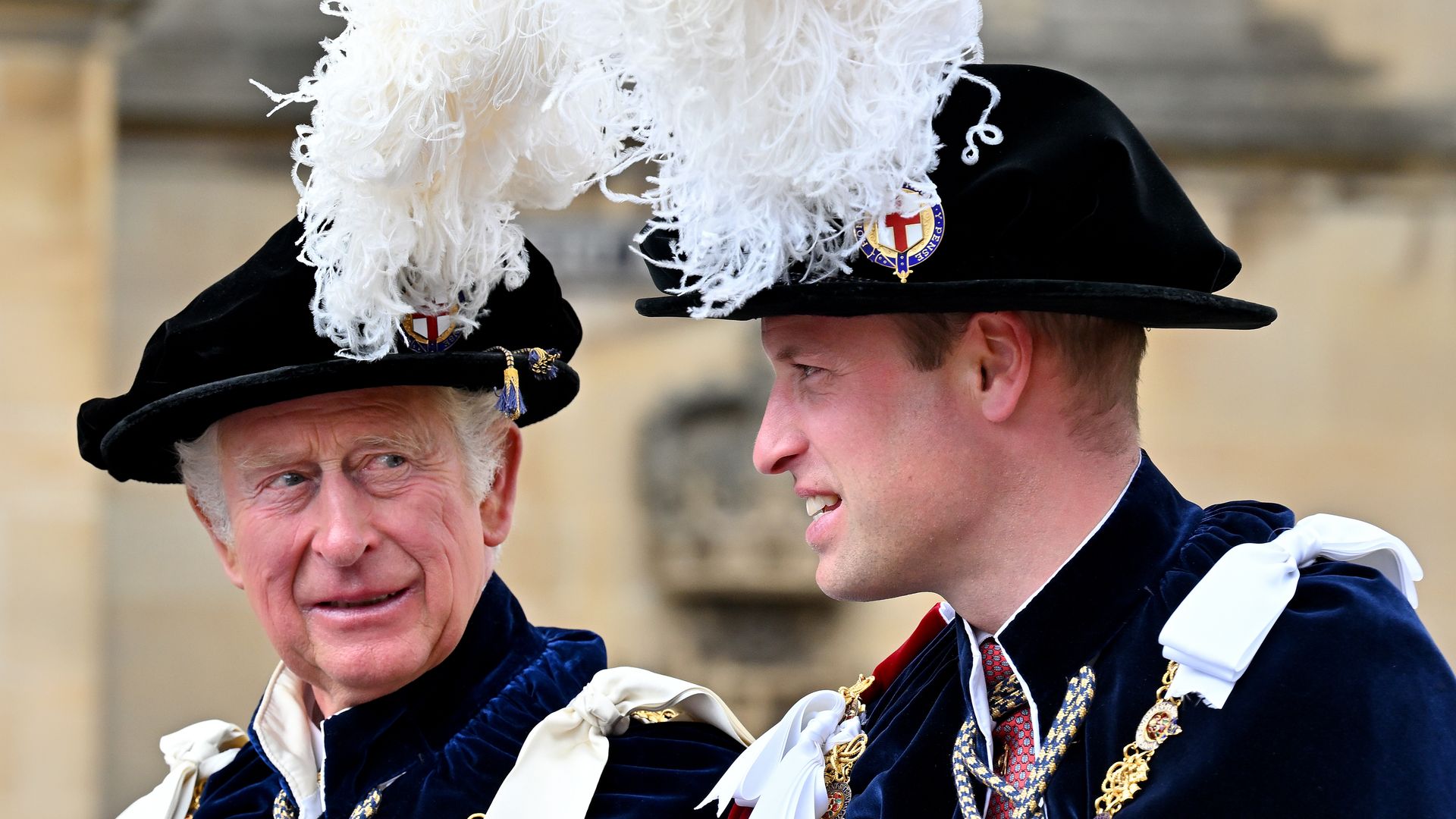 King Charles and Prince William smiling together in feathery hats