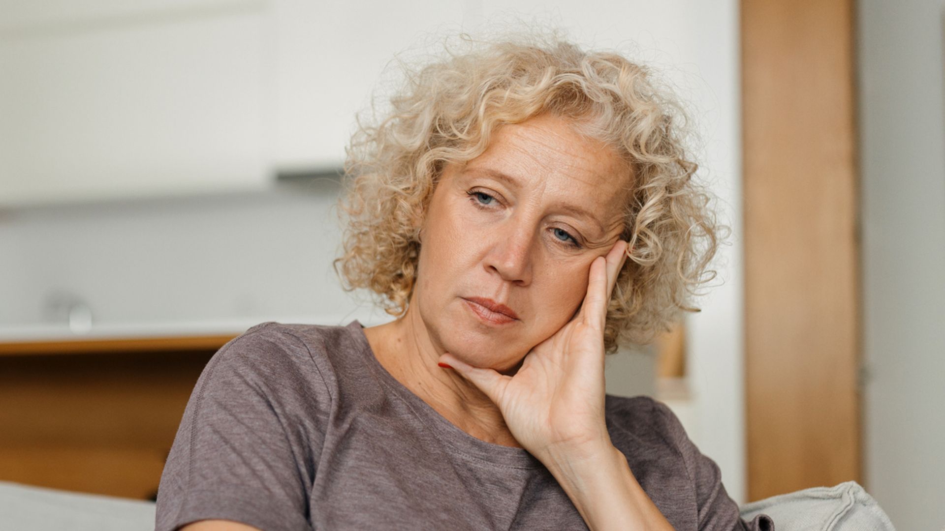 A senior woman, aged 50-54, finds solace on the sofa during winter. She is worried and has sad face