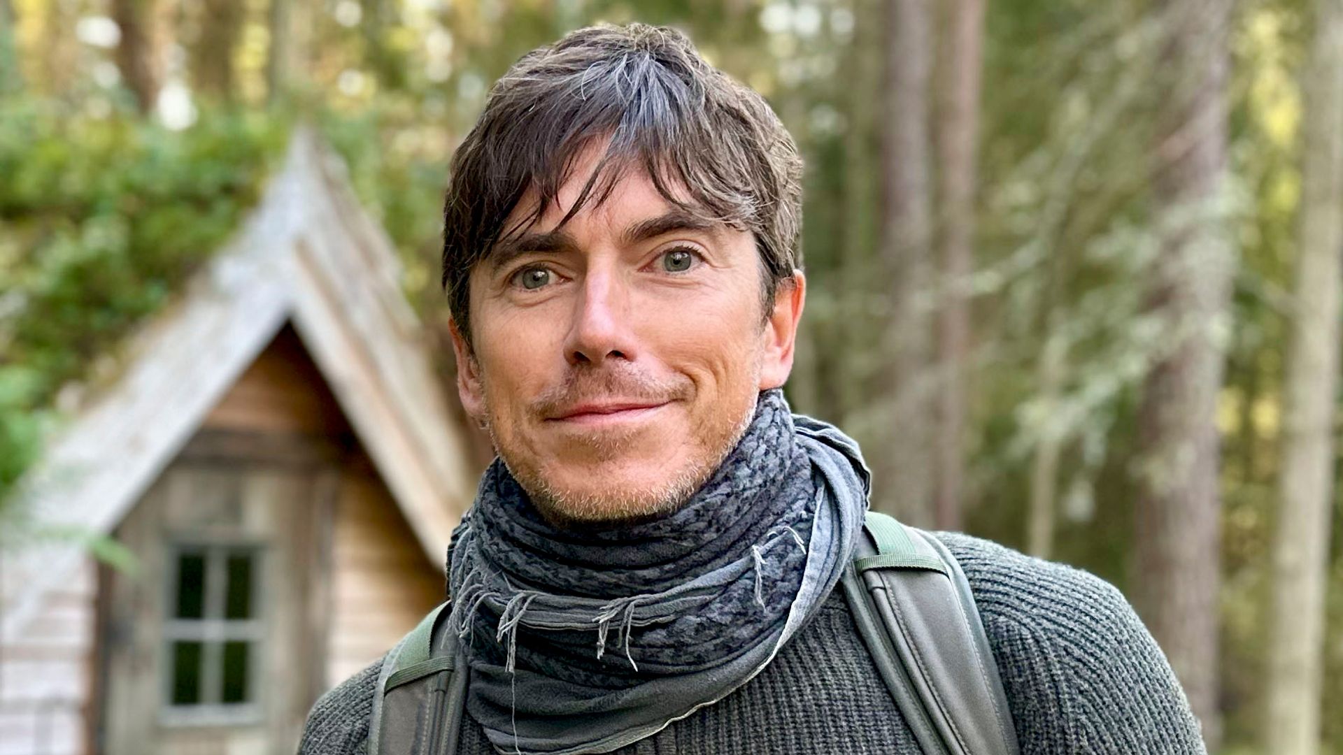 Simon Reeve standing in front of a wooden cabin