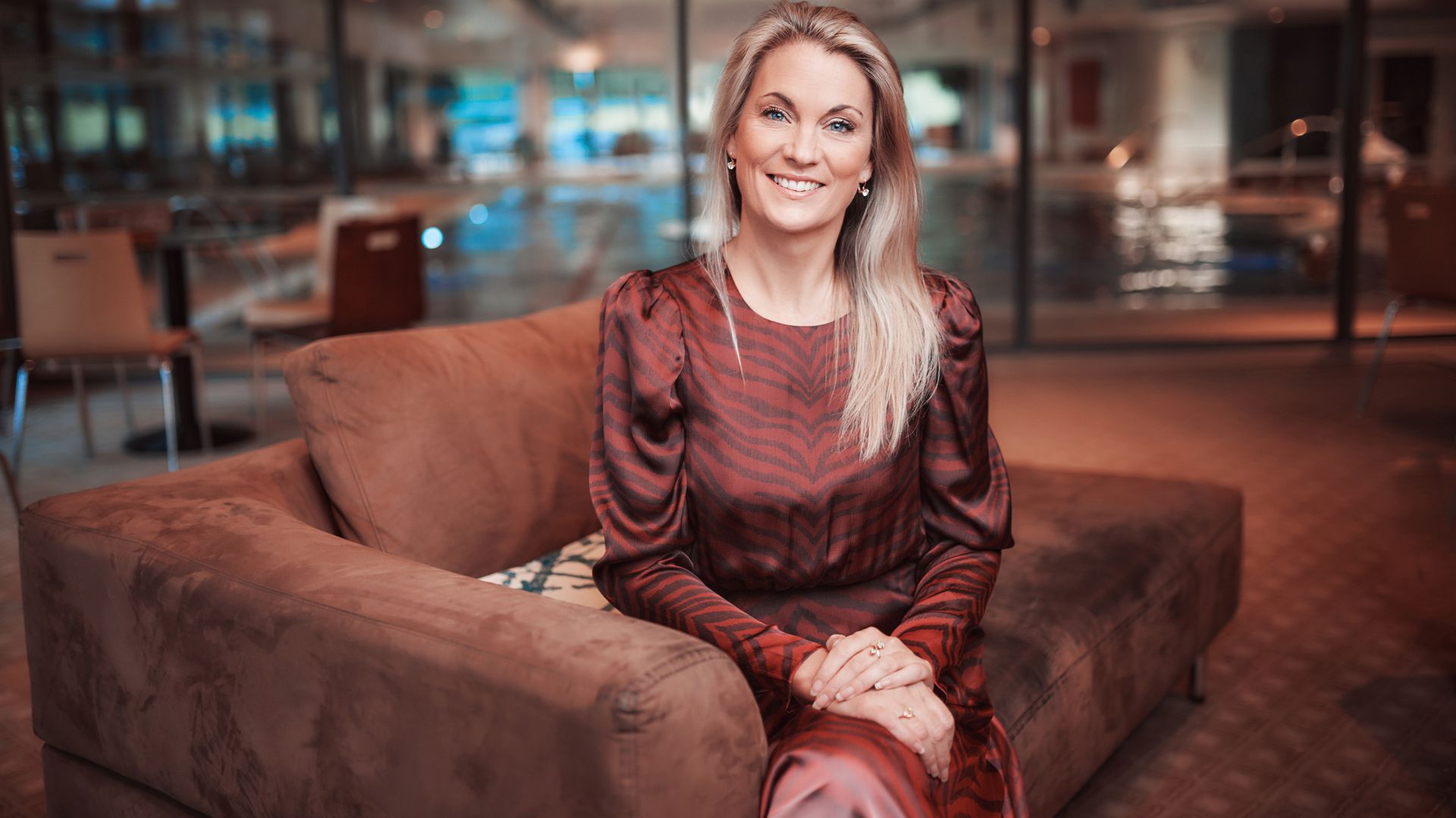 blonde woman in a zebra print dress smiling on a brown sofa 
