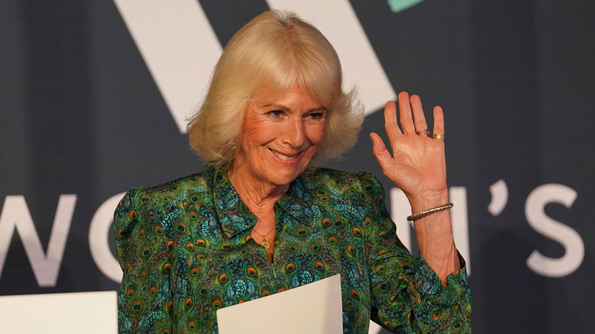 Queen Camilla waving to a crowd following a speech
