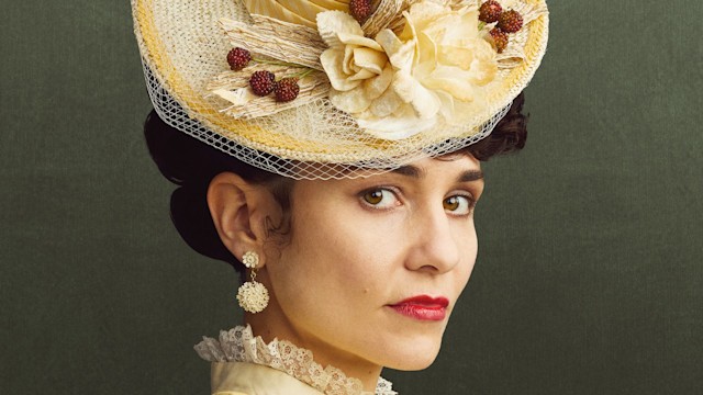 woman in yellow period clothing and hat against green background