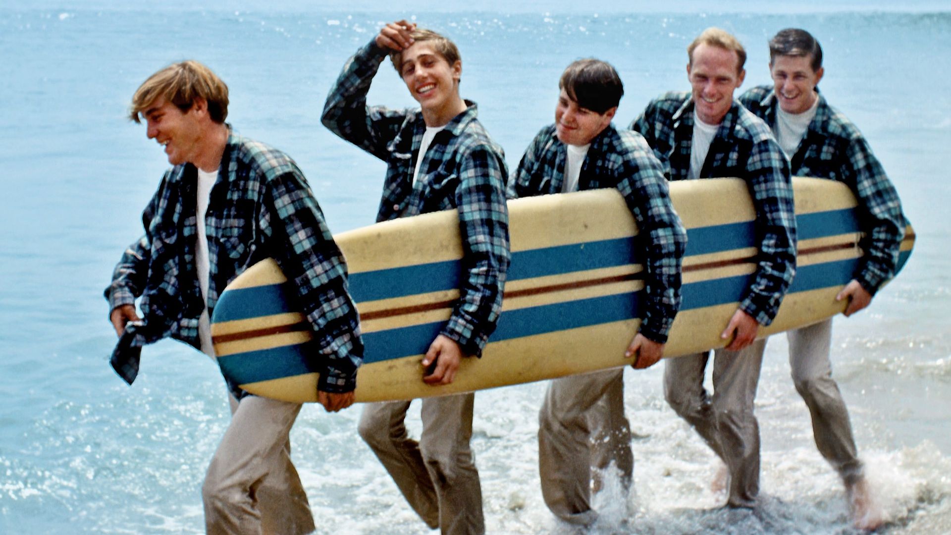 the beach boys on a beach holding a surfboard