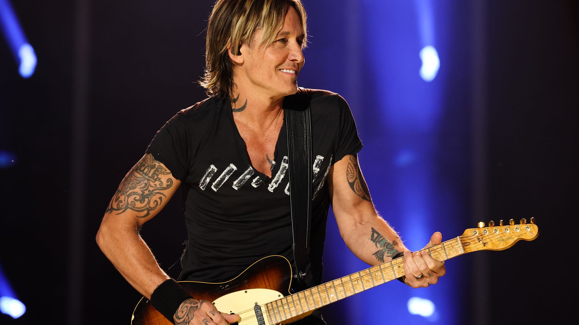 Keith Urban performing on stage with a guitar, looking to the right