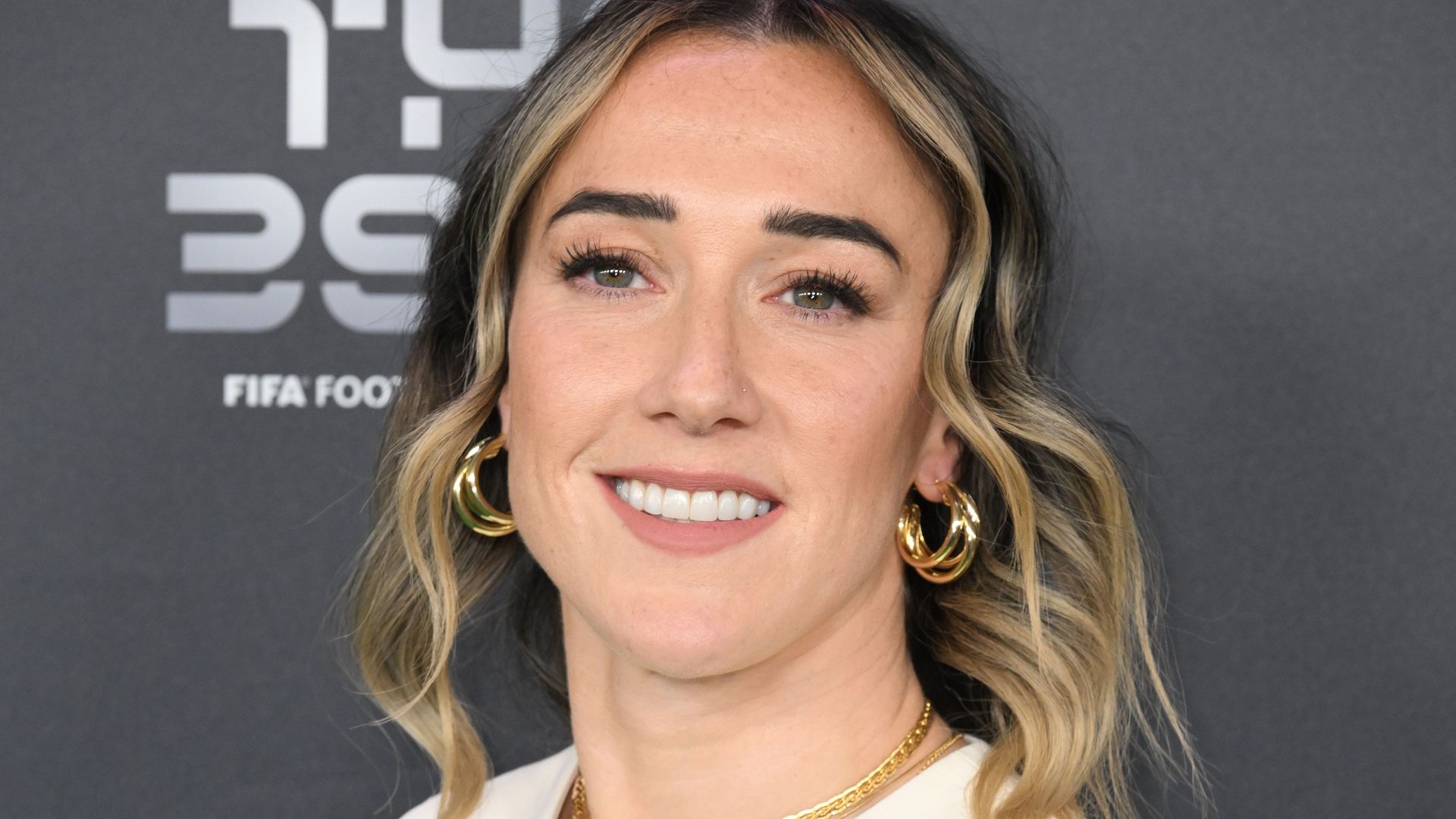 Lucy Bronze with curly hair in a cream waist coat