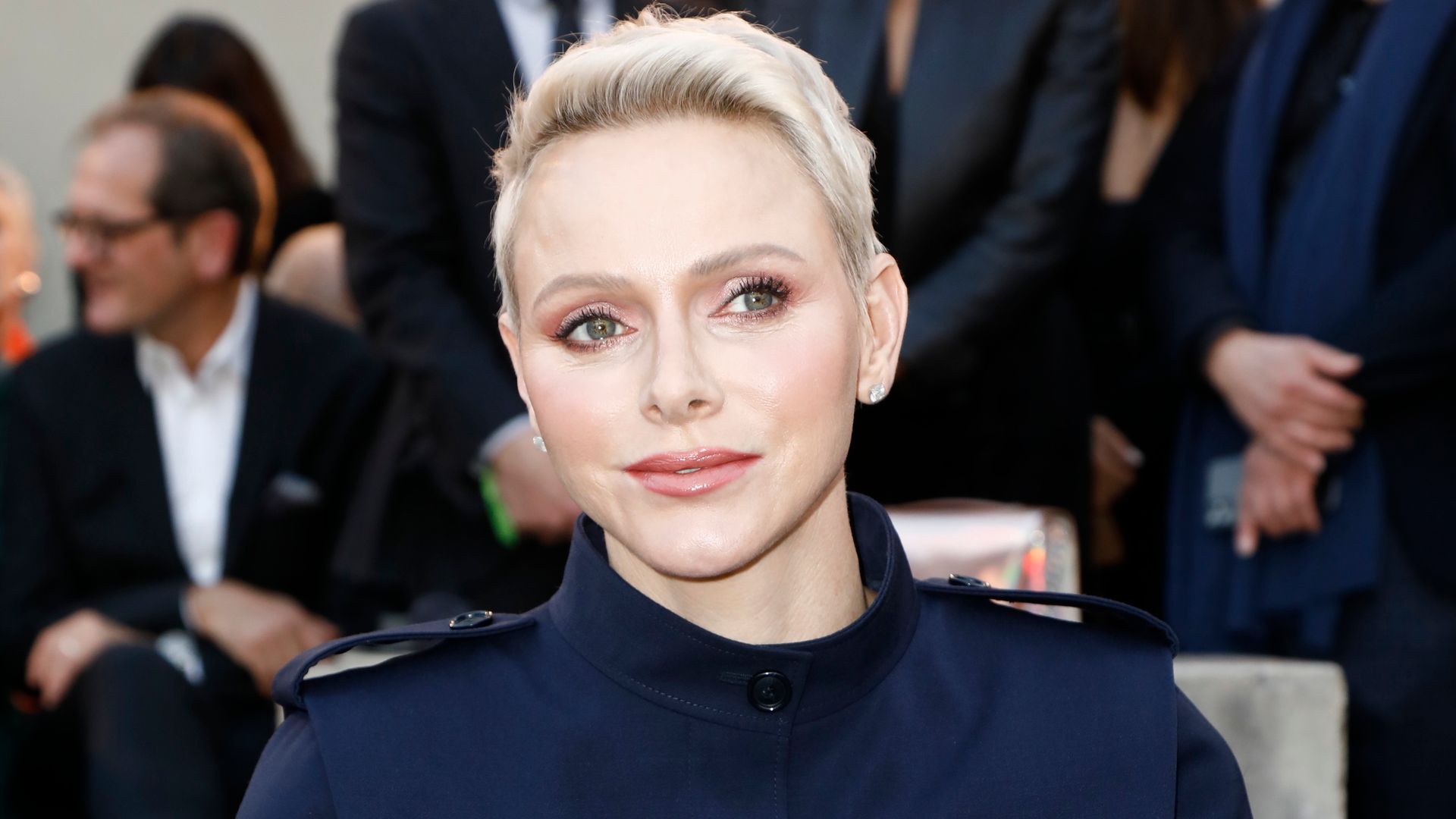 Princess Charlene wearing a navy suit whilst holding a programme at Paris Fashion Week