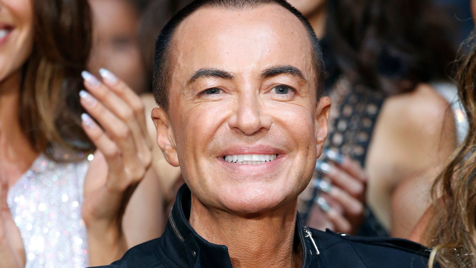 Julien Macdonald smiling as people applaud his fashion show around him