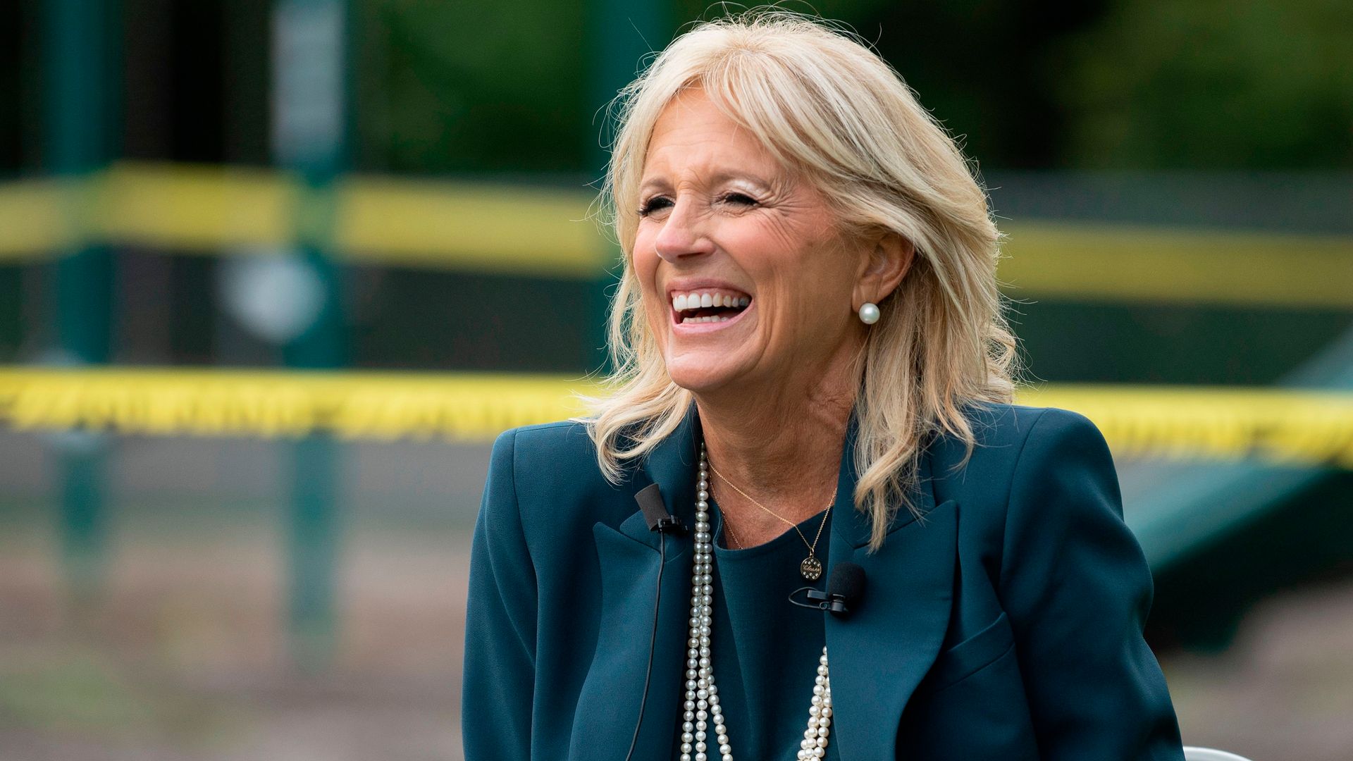 Jill Biden smiling in a teal suit and a pearl necklace