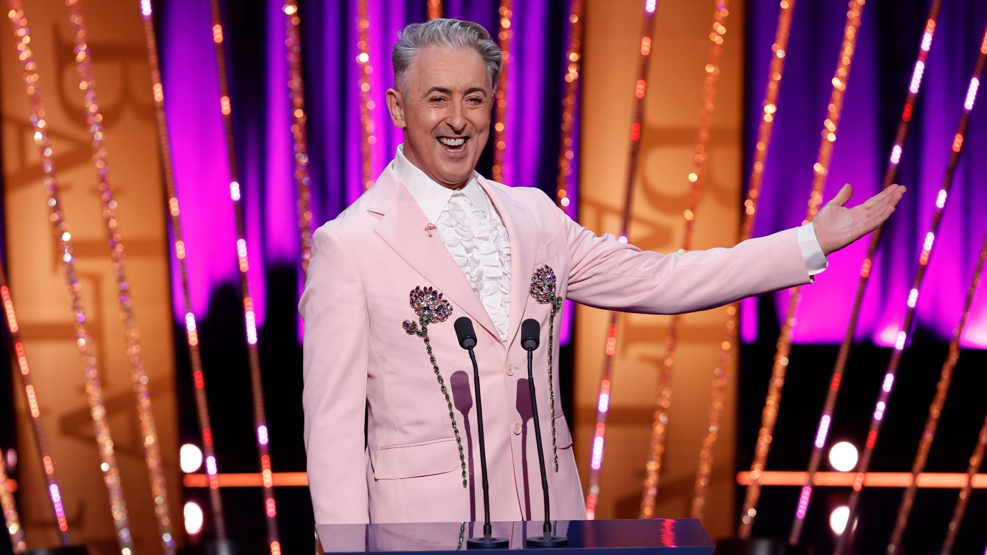 TV host on stage at awards ceremony in pink suit